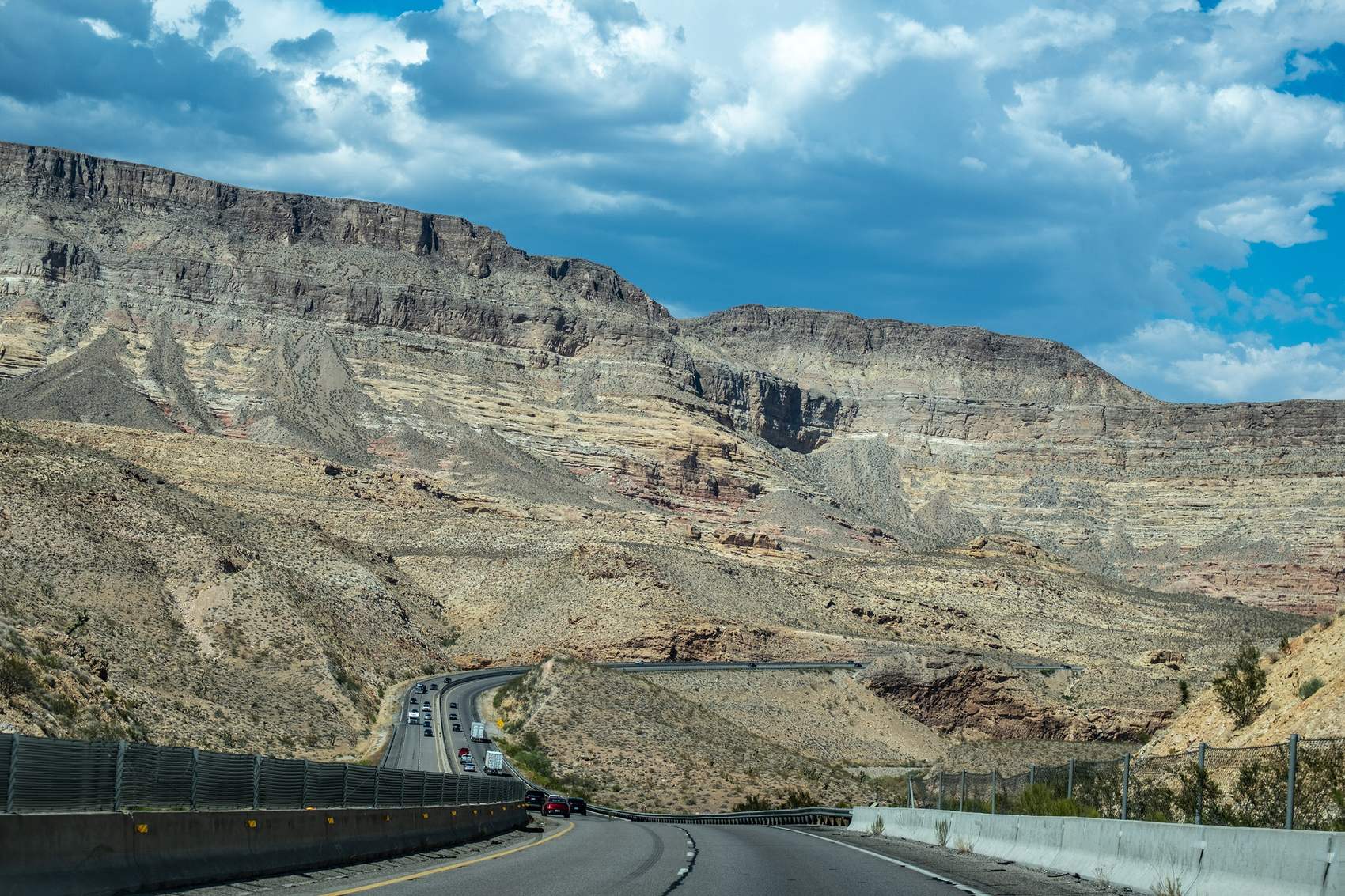 Interstate 15 curving through the Virgin River Gorge beneath layered desert cliffs and a dramatic cloudy sky