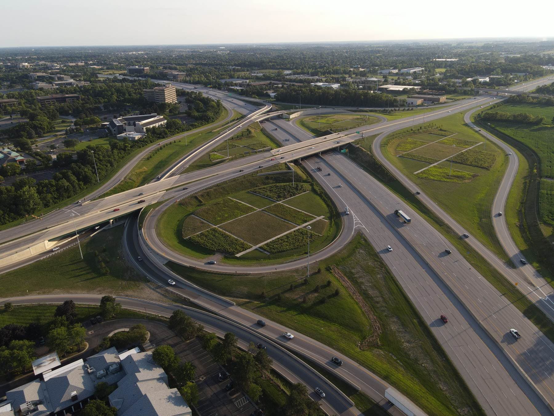 An aerial view of a cloverleaf interchange where an interstate highway meets a state route, with green loops and ramps in late-afternoon light