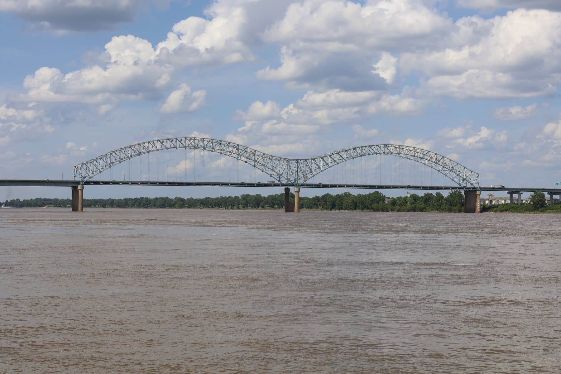 The twin steel arches of the Interstate 40 bridge spanning the wide Mississippi River under a sky of white clouds